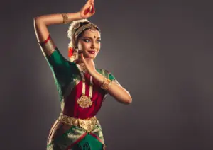 A dancer in traditional attire gracefully poses against a neutral background, showcasing vibrant colors.