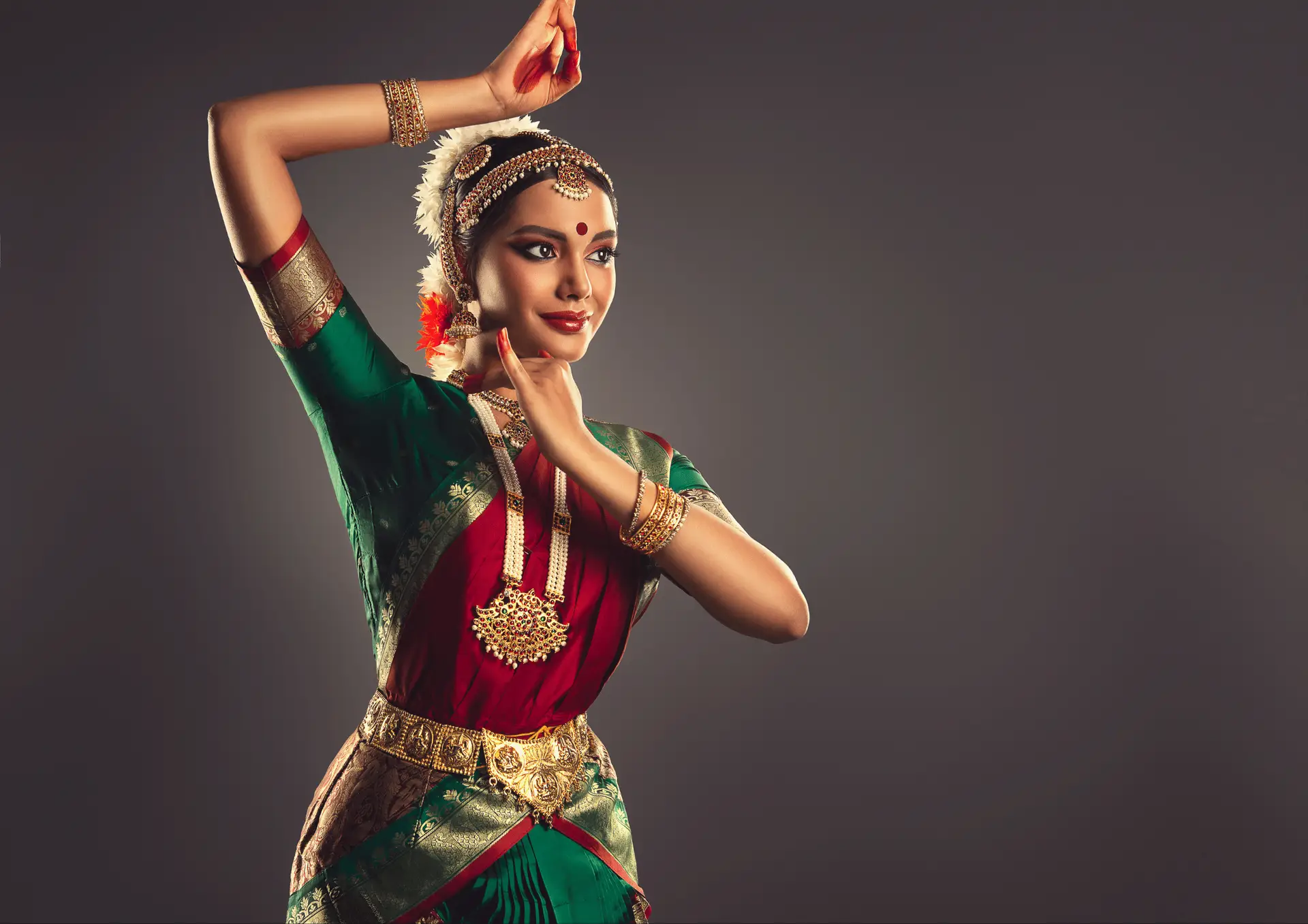 A dancer in traditional attire gracefully poses against a neutral background, showcasing vibrant colors.