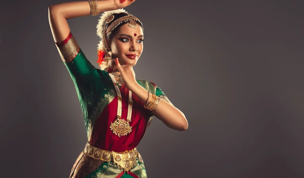 A dancer in traditional attire gracefully poses against a neutral background, showcasing vibrant colors.