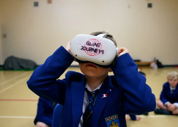 Child in a blue blazer wearing a VR headset with "Giant Journeys" written on it.