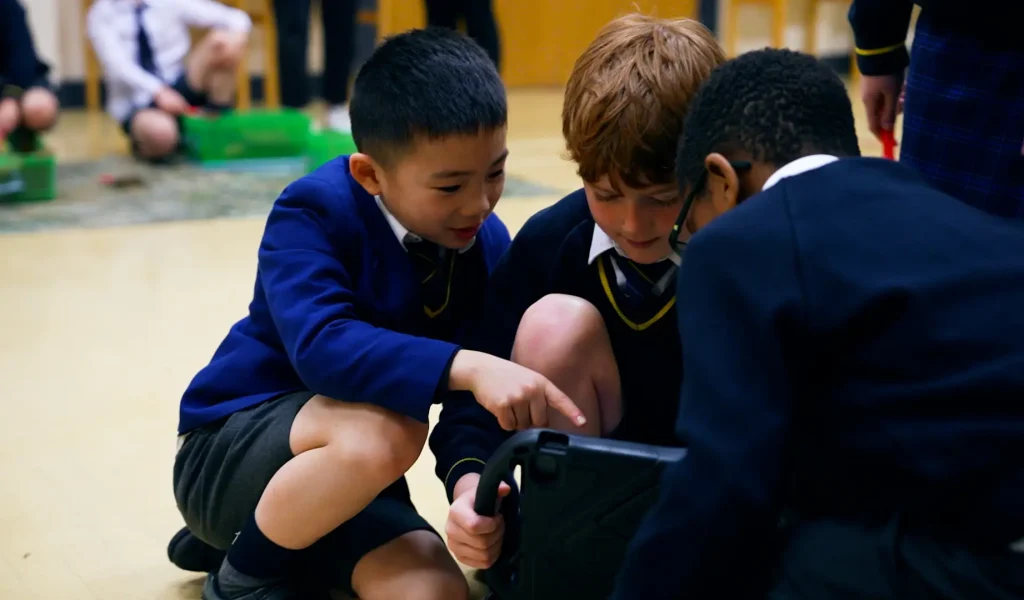 Three children gather around a device, engaged in exploration and conversation.